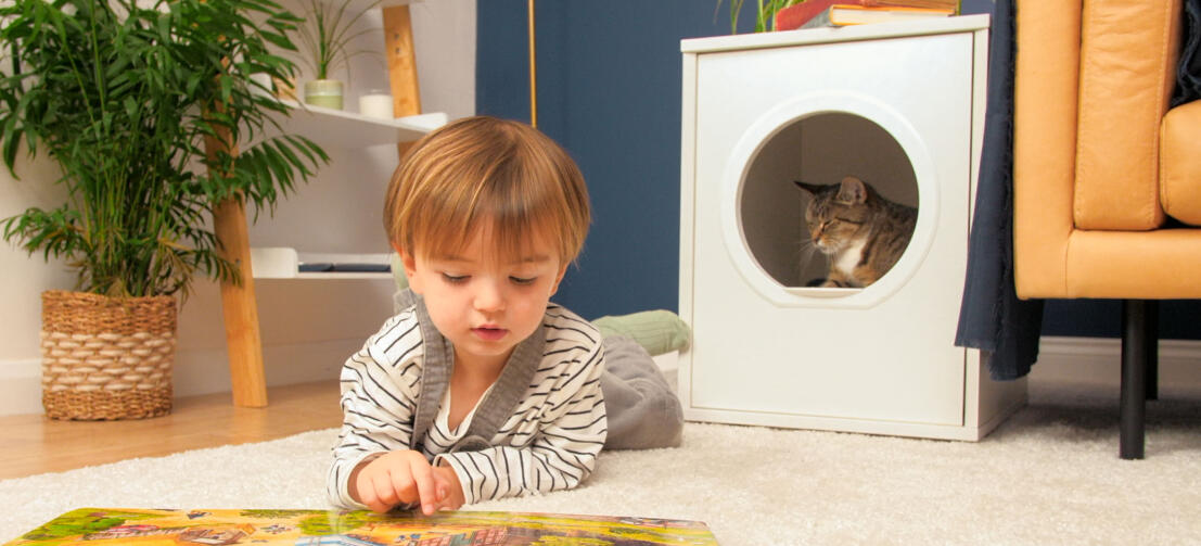 Katt sitter i privat og moderne hi-møbler Maya kattehus med barn som legger seg foran og leser en bok