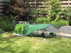 Un poulailler vert et un parcours avec couverture, dans un jardin
