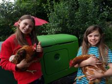 Twee meisjes met kippen naast hun kippenhok