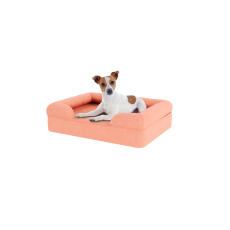 Perro sentado en una pequeña cama de espuma de memoria de color rosa melocotón