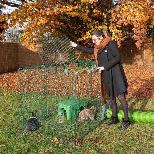 a woman opening a rabbit run with the zippi easy locks with a zippi tunnel and shelter inside
