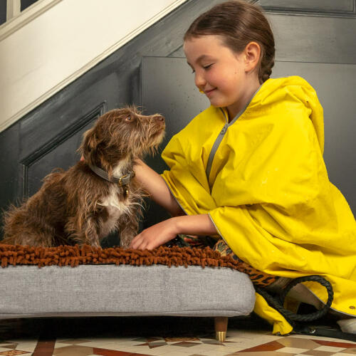 Cane accarezzato da ragazza mentre su Omlet Topology letto per cani con topper in microfibra e piedini in legno con tappo in ottone