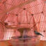 Un modelo de pájaro posado en un comedero dentro de una jaula rosa con un espejo