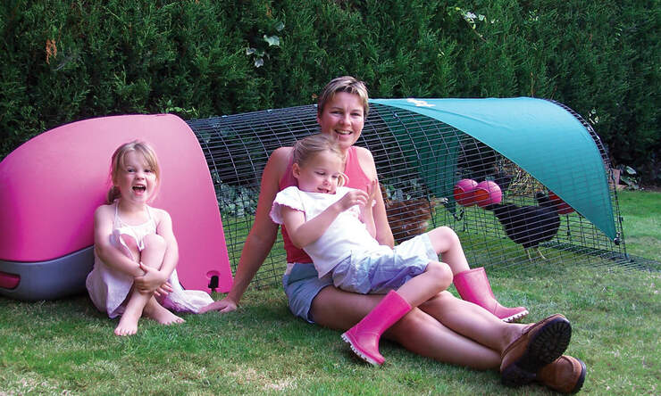 A family with their pink Eglu Classic plastic chicken coop with run