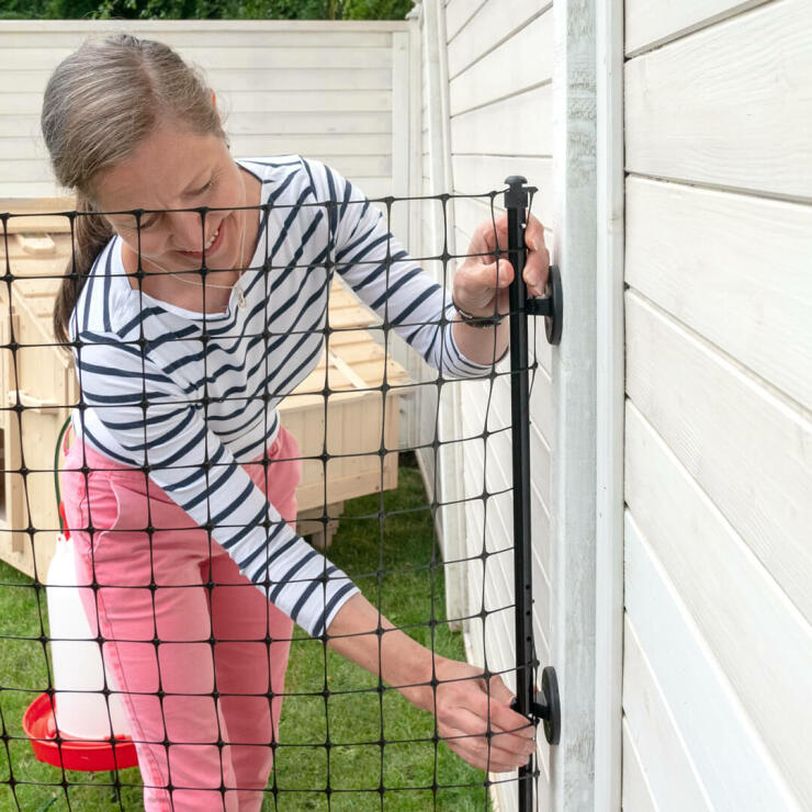 A woman attaching chicken fencing to a shed wall.