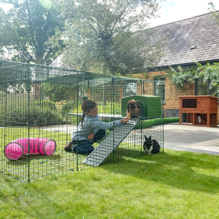 Two rabbits with girl in Omlet Zippi Rabbit Playpen with Green Zippi Shelter and Zippi Platforms