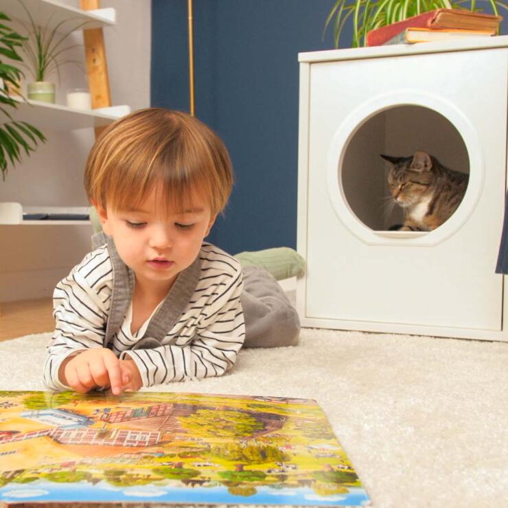 Katt sitter i privat og moderne hi-møbler Maya kattehus med barn som legger seg foran og leser en bok
