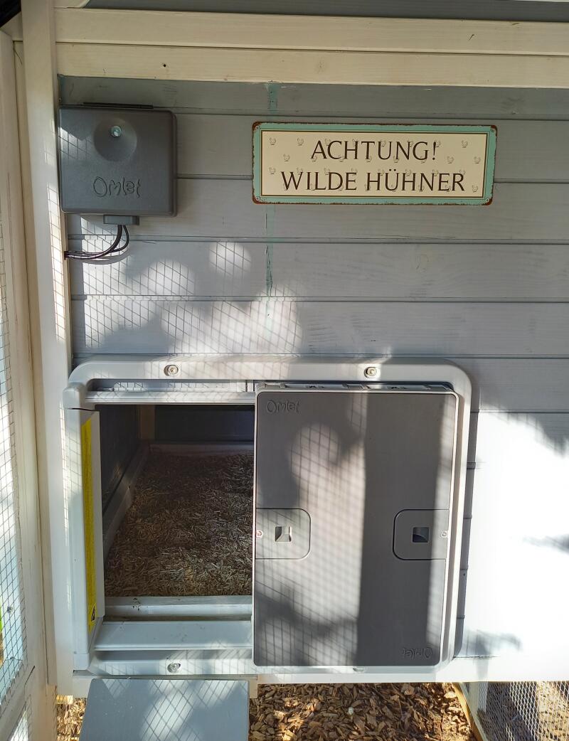 A grey automatic door mounted on a grey wooden chicken coop