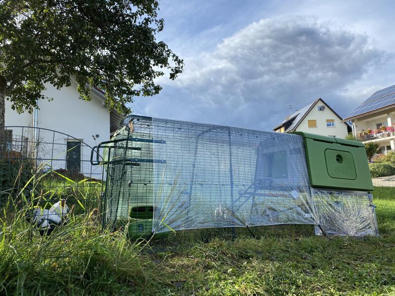 A chicken coop and run with handles on the end of the run, covered by transparent tarpaulins