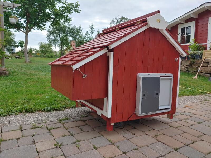 A red wooden chicken coop with a grey automatic door