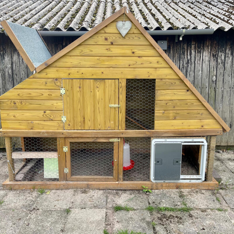 A grey automatic coop door mounted on chicken fence