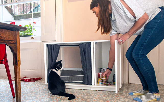 Un mueble-casa para gatos Maya Nook con el armario abierto y un gato mirando