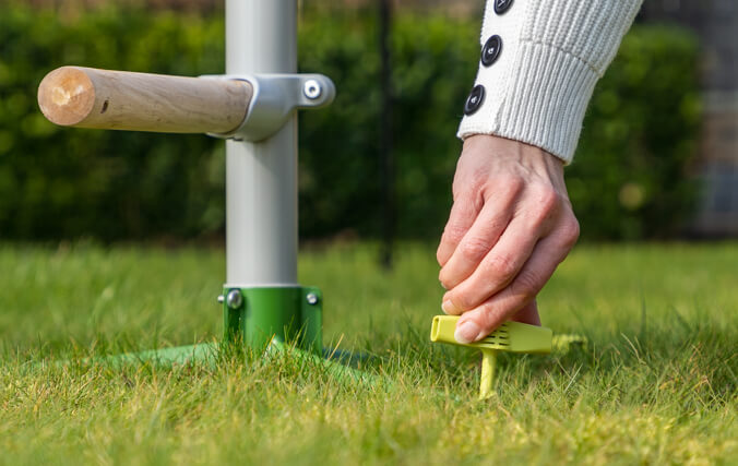 Kobieta mocuje wolnostojącą grzędę na trawniku za pomocą łatwych w użyciu wkręcanych kołków