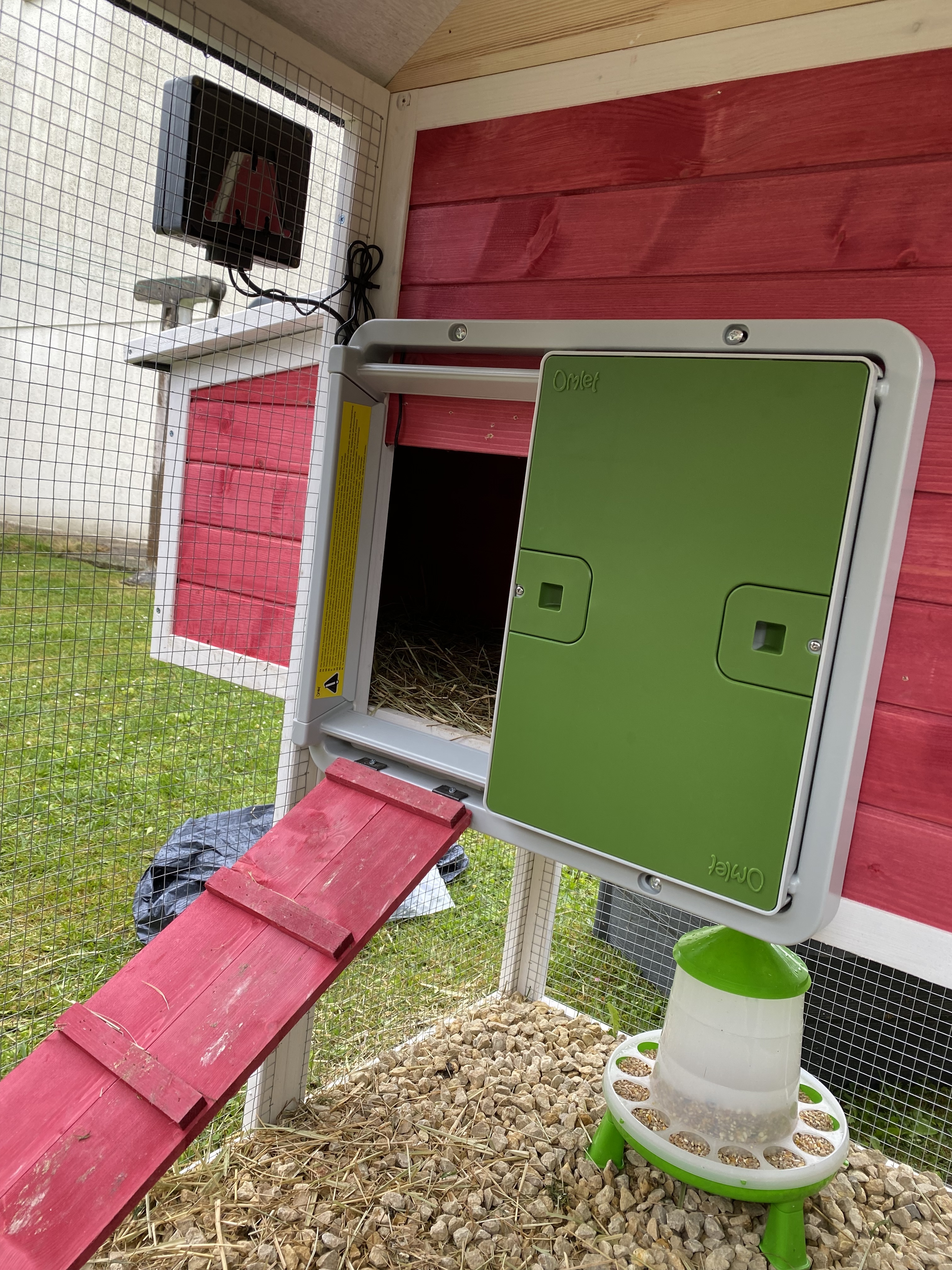 A green automatic coop door mounted on a red wooden coop